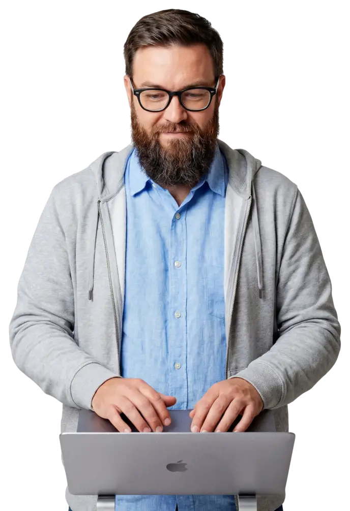 usecases-protect-hero-p4 A professional man with glasses and a beard typing on a laptop, wearing a gray hoodie over a blue shirt